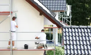 Dwóch malarzy na rusztowaniu odnawia elewację domu. Sprawdź, jaka jest malowanie elewacji cena.