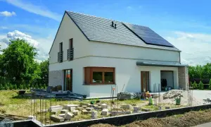 Nowy dom w trakcie budowy, z panelami słonecznymi na dachu. Rozbudowa domu postępuje, widać materiały budowlane i fundamenty.