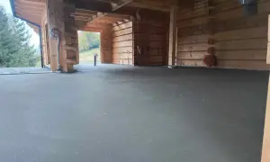 Wnętrze drewnianego domu w budowie. Na pierwszym planie świeżo wylany, szary miksokret. W tle widoczne drewniane ściany i belki stropowe.
