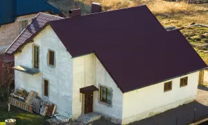 Nowy dom w zabudowie zagrodowej z ciemnobordową dachówką, w trakcie budowy.