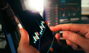 Dłoń trzyma smartfon z wykresem świecowym, pokazującym wibor 3m aktualny. W tle widać inne wykresy finansowe.