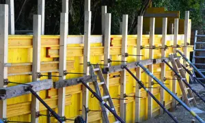 Żółty szalunek budowlany z drewnianymi słupkami i metalowymi podporami, gotowy do zalania betonem.