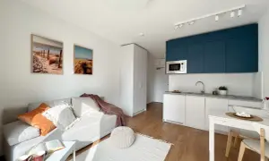 Nowoczesne mieszkanie w Warszawie: salon z sofą, kuchnia z niebieskimi szafkami i jadalnia. Idealne miejsce, by снять квартиру в Варшаве.