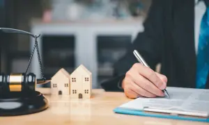 Prawnik podpisuje umowę dożywocia, symbolizowaną przez drewniane domki i wagę sprawiedliwości.