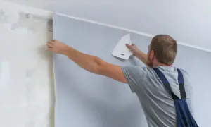Mężczyzna przykleja tapetę, wygładzając ją pacą. Sprawdź, jaka jest tapetowanie cena i odmień swoje wnętrze!