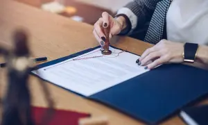 Kobieta pieczętuje dokument, prawdopodobnie umowę przedwstępną. Na stole leży też pióro i symbol sprawiedliwości.
