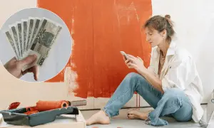 Kobieta planuje remont mieszkania, przeglądając telefon. W tle widać farbę i wałek, a w rogu zdjęcie pieniędzy, sugerujące dotację na remont mieszkania.