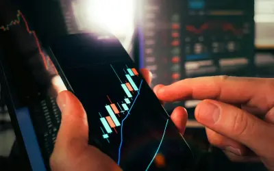 Dłoń trzyma smartfon z wykresem świecowym, pokazującym wibor 3m aktualny. W tle widać inne wykresy finansowe.