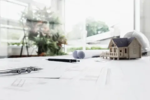 Na stole architekta: makieta domu, cyrkiel, ołówki i plany, które wyznaczają nieprzekraczalna linia zabudowy.