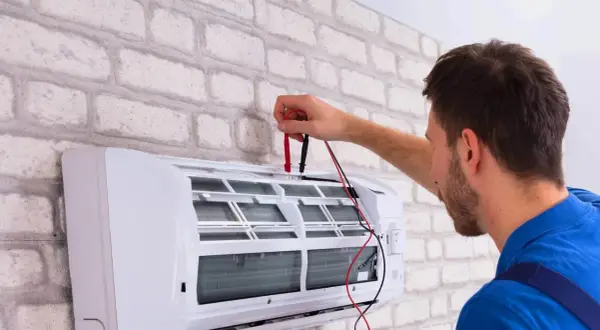 Sprawdź, jaka jest odgrzybianie klimatyzacji cena. Technik z miernikiem przy białej jednostce klimatyzacyjnej.