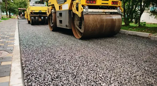 Walec drogowy ubija świeży asfalt. Prace drogowe w toku, pospółka czeka na wyrównanie.