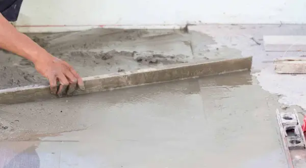 Ręka pracownika wykonuje zacieranie betonu za pomocą łaty.