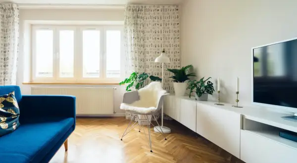 Jasny salon po remoncie starego domu. Błękitna kanapa, białe meble, parkiet i rośliny tworzą przytulną atmosferę.
