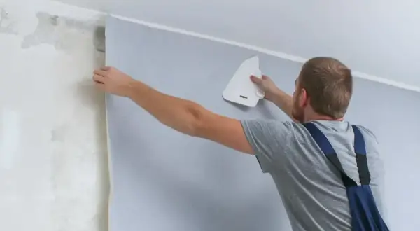 Mężczyzna przykleja tapetę, wygładzając ją pacą. Sprawdź, jaka jest tapetowanie cena i odmień swoje wnętrze!