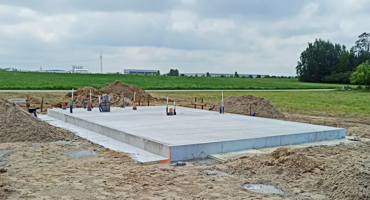 Gotowy betonowy fundament na placu budowy. Widać rury i zbrojenie. Cena budowy fundamentów zależy od wielu czynników.