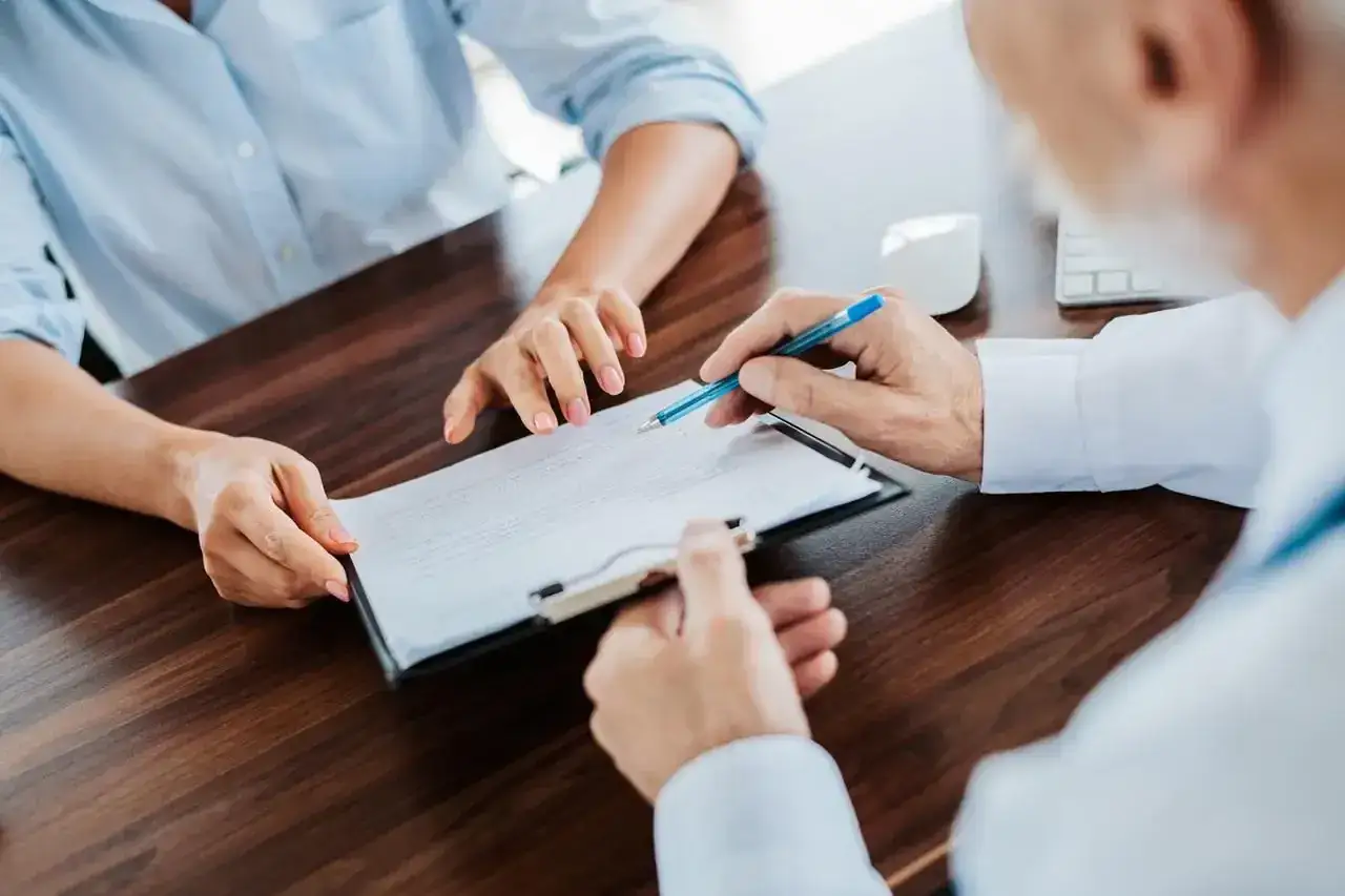 Doradca finansowy omawia z klientką warunki restrukturyzacji kredytu. Dłonie wskazują na dokumenty na biurku.