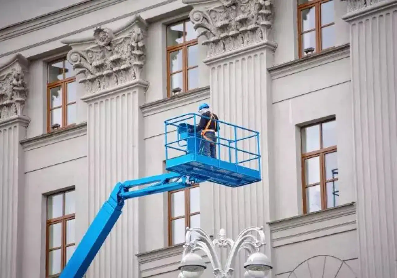 Pracownik w podnośniku koszowym wykonuje prace elewacyjne, być może związane z renowacją fasady z użyciem wapna palonego.