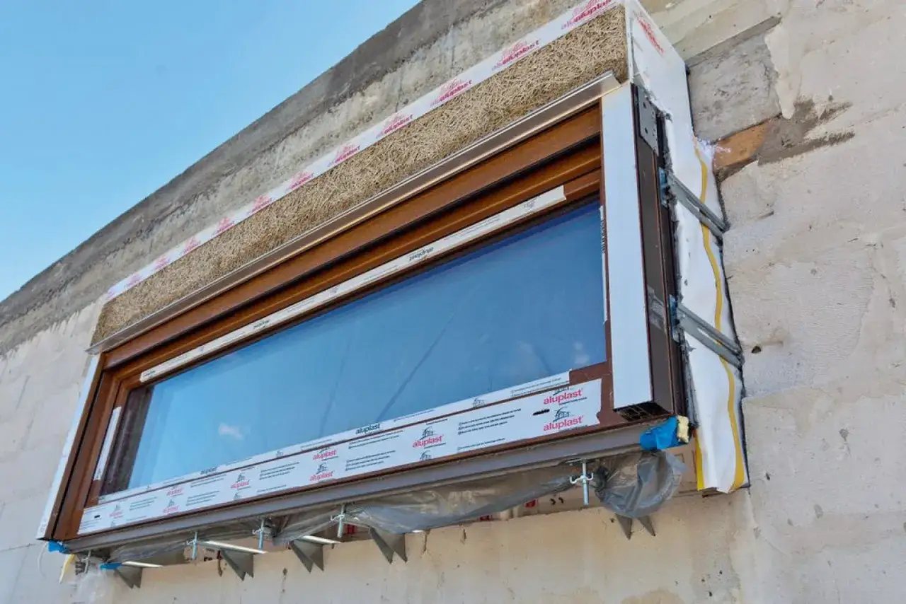 Montaż okna z wykorzystaniem wełny drzewnej jako izolacji. To kluczowy etap termomodernizacji budynku, zapewniający oszczędność energii.