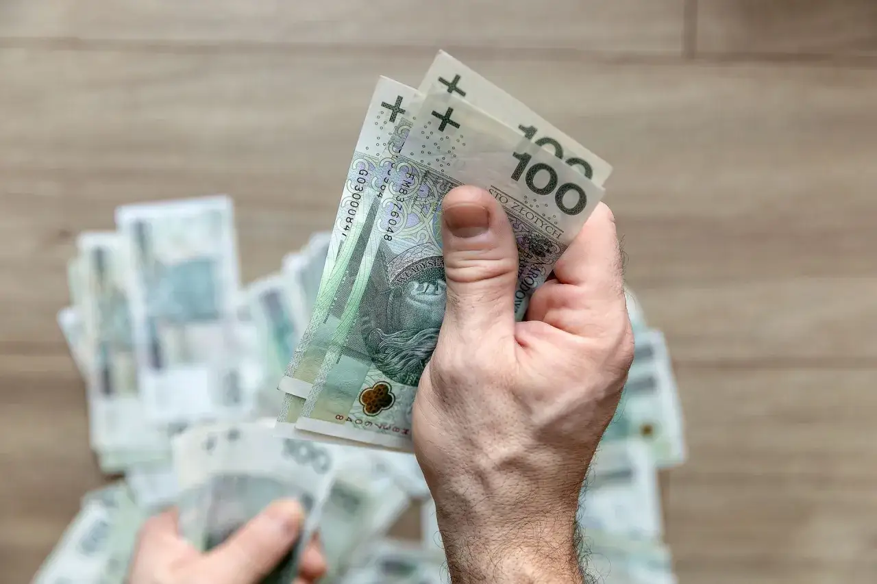 Dłoń trzyma banknoty 100 zł. Zastanawiasz się, ile wynosi podatek od darowizny 100 tys.?