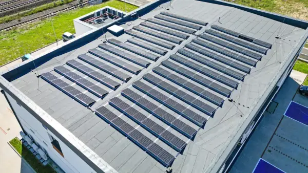 Duży płaski dach pokryty panelami fotowoltaicznymi, które zbierają energię słoneczną.