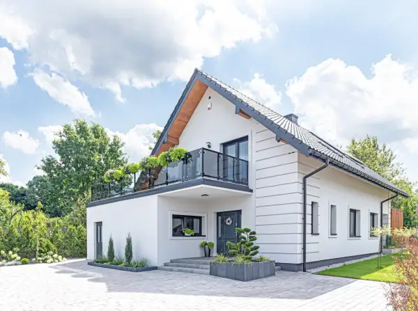 Nowoczesny biały dom z balkonem i zielenią. Idealny przykład darmowych projektów domów, które inspirują do budowy.