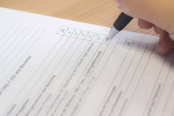 Ręka z długopisem zaznacza zielone ptaszki na dokumencie. To protokół zdawczo odbiorczy, który potwierdza wykonanie czynności.