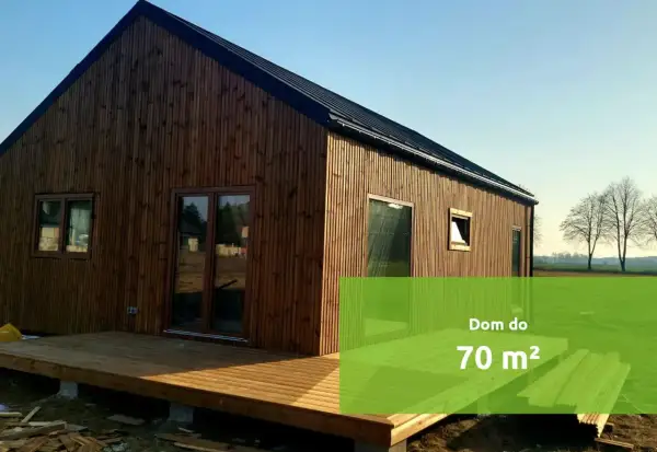Drewniany budynek gospodarczy z tarasem, w tle pole i drzewa. Idealny na mały dom do 70 m².
