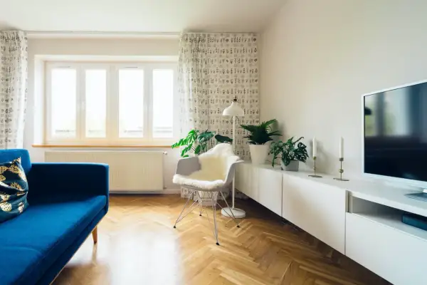 Jasny salon po remoncie starego domu. Błękitna kanapa, białe meble, parkiet i rośliny tworzą przytulną atmosferę.