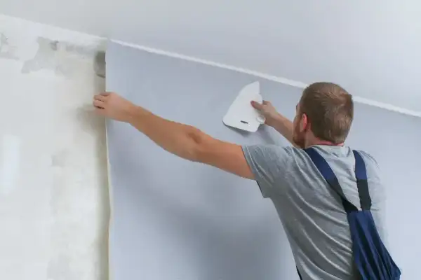 Mężczyzna przykleja tapetę, wygładzając ją pacą. Sprawdź, jaka jest tapetowanie cena i odmień swoje wnętrze!