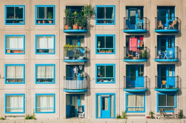 Elegancka loggia i balkon z niebieskimi ramami okiennymi, pełne zieleni i suszącego się prania, tworzą kolorowy obraz miejskiego życia.